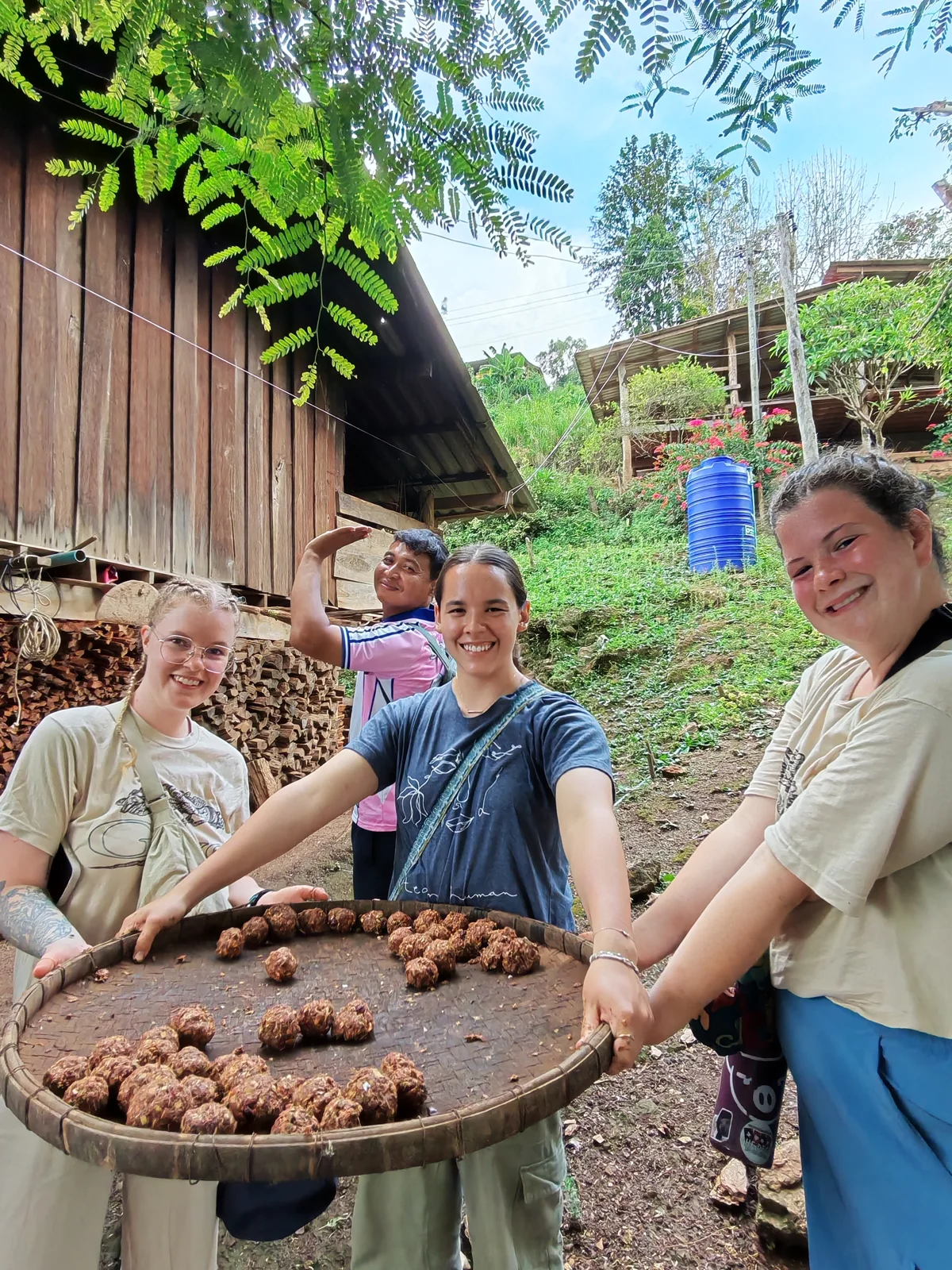 Three participants holding a woven tray of produce outside a village building