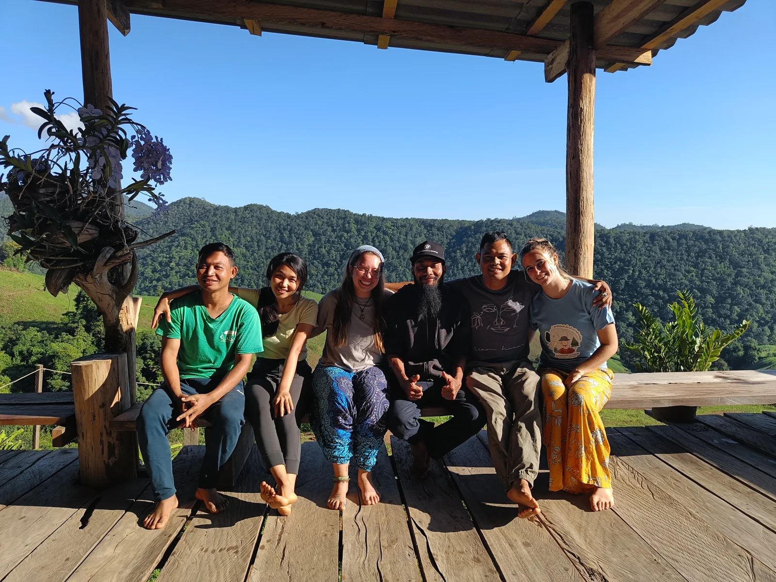 A small group sitting together on a wooden terrace overlooking green hills