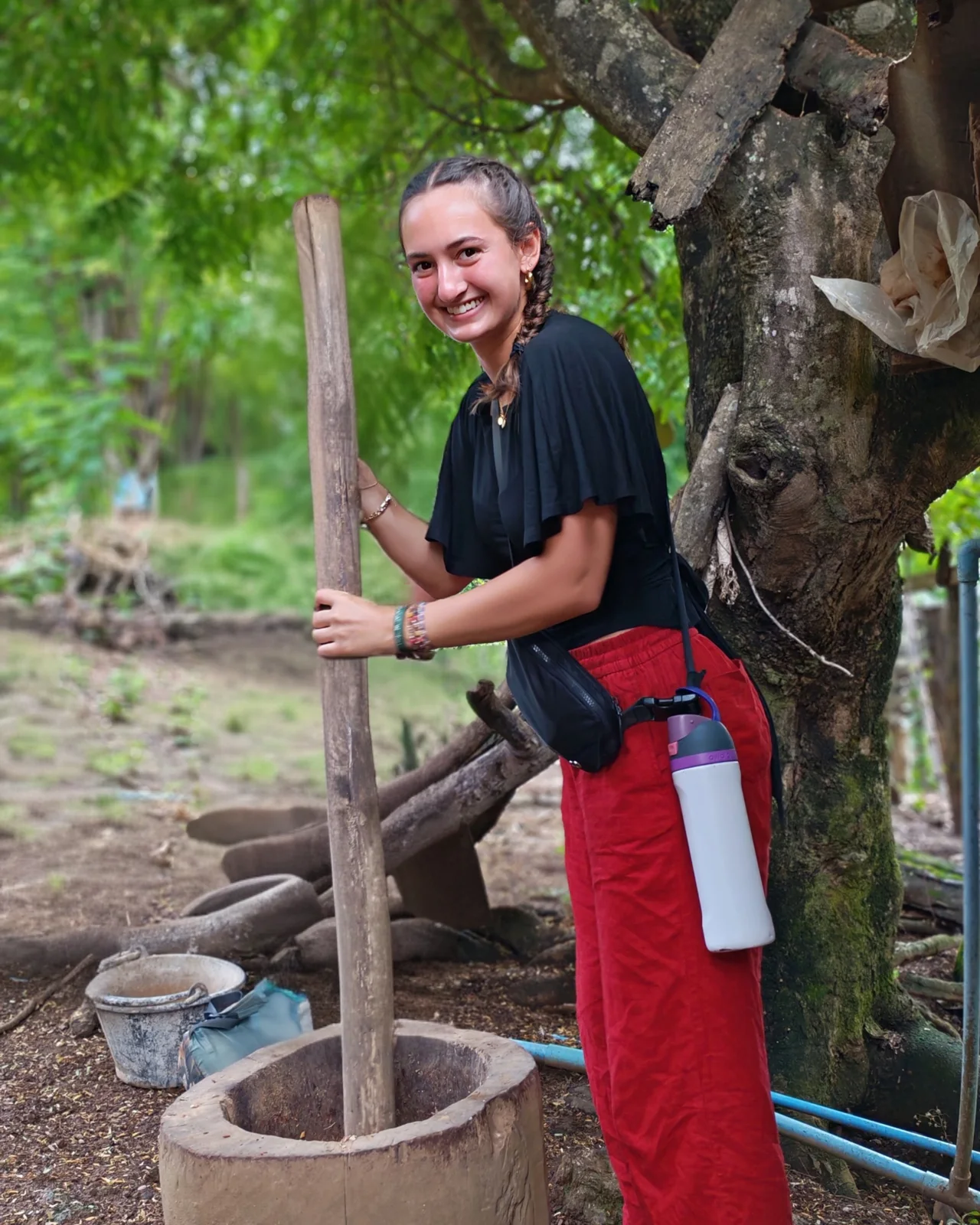 A participant using a large wooden pestle beside a village building